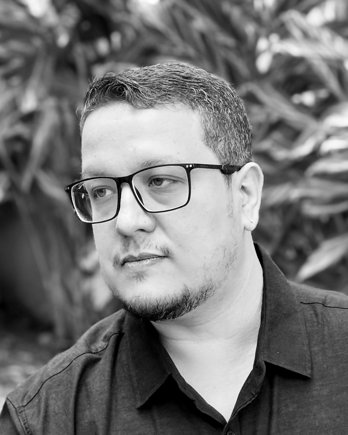 Retrato documental em preto e branco de Mateus Fardin, de camisa escura e óculos, olhando para a esquerda.